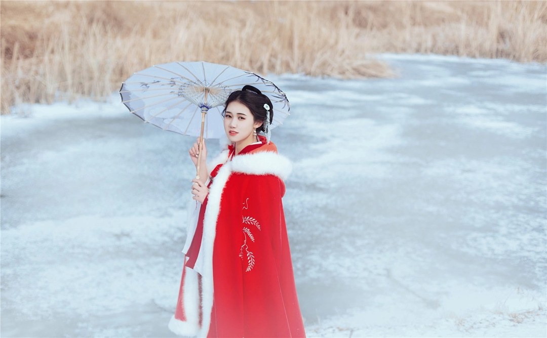 雪地红斗篷少女撑白伞，花簪垂珠与毛绒镶边清冷出镜