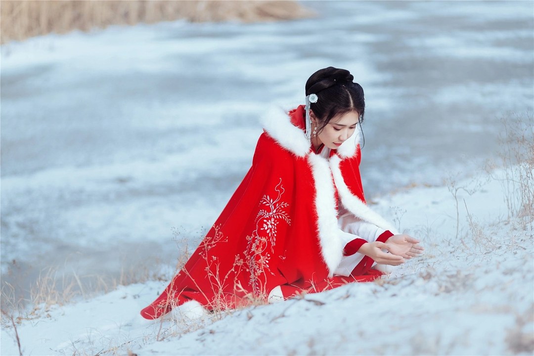 雪地红斗篷少女撑白伞，花簪垂珠与毛绒镶边清冷出镜